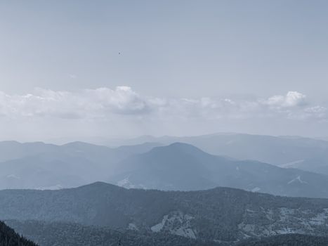 From above of picturesque mountain with trees in mist under gray cloudy sky