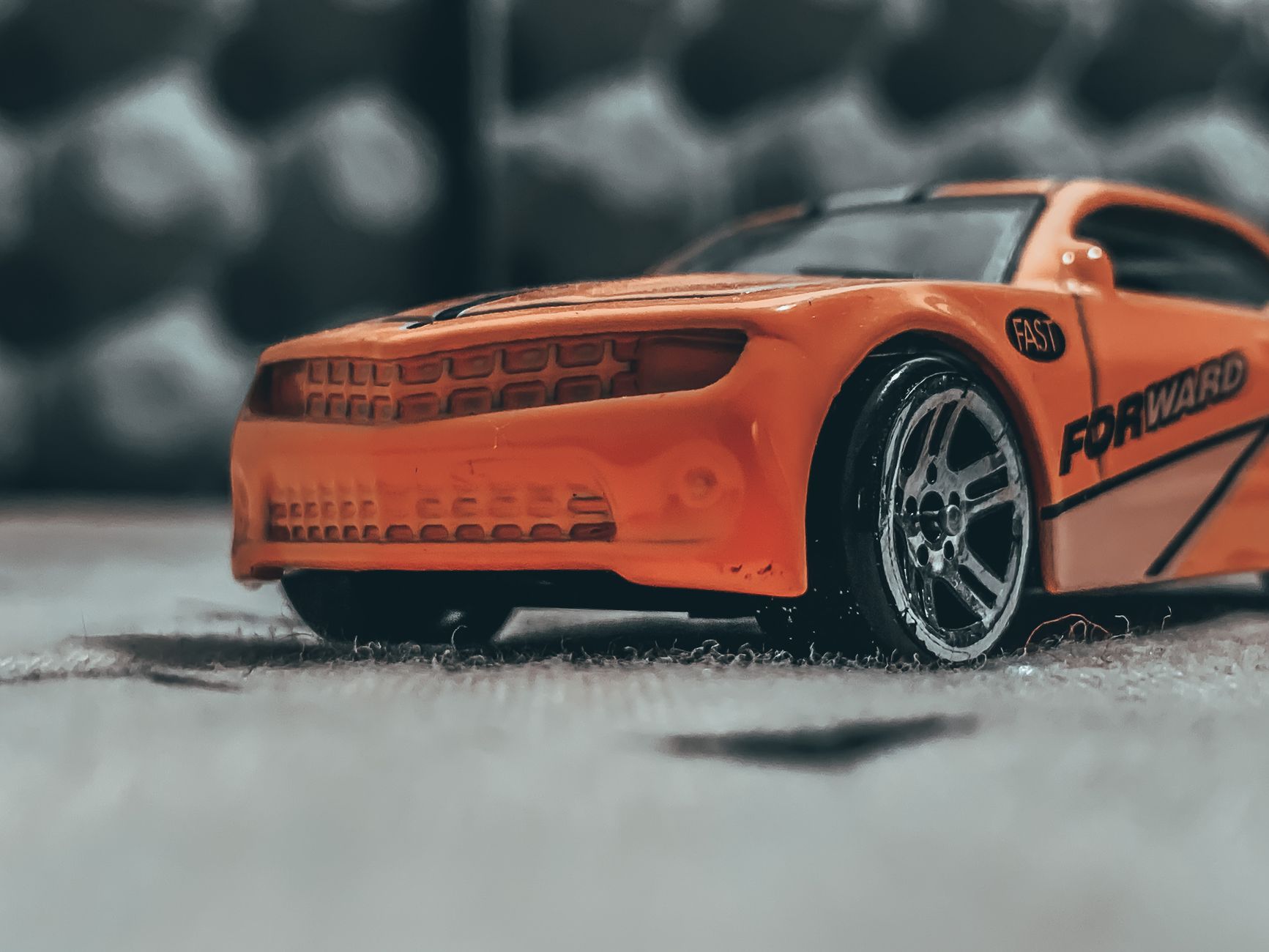 Orange contemporary toy car with sticker placed on dusty floor in soft focus