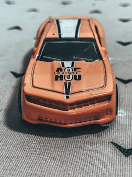 From above of small miniature of weathered orange toy car placed on rough carpet