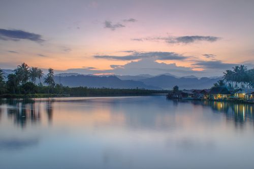 Free Peaceful lake scene at sunset with mountains and palm trees reflected on water. Stock Photo