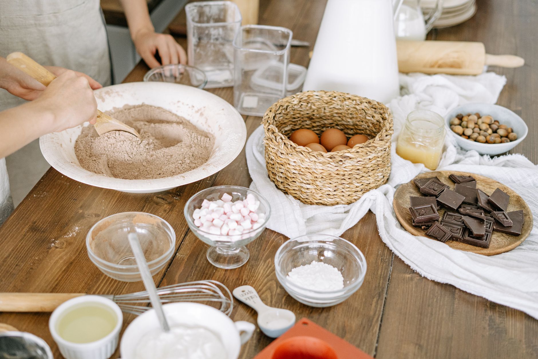 Close-up of hands mixing baking ingredients on a wooden table indoors.
