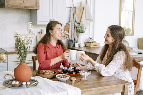 Free Two women sharing coffee and muffins at a cozy kitchen table, enjoying a relaxing morning together. Stock Photo