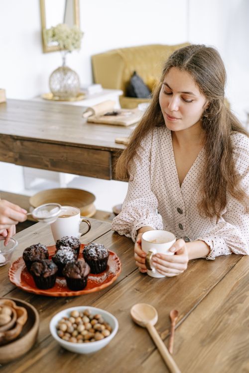 Free A young woman savoring coffee with chocolate muffins at a cozy kitchen table. Stock Photo
