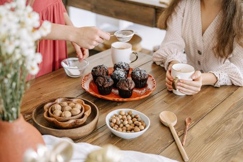 Free A cozy morning scene with chocolate muffins, coffee, and conversation at a wooden table. Stock Photo