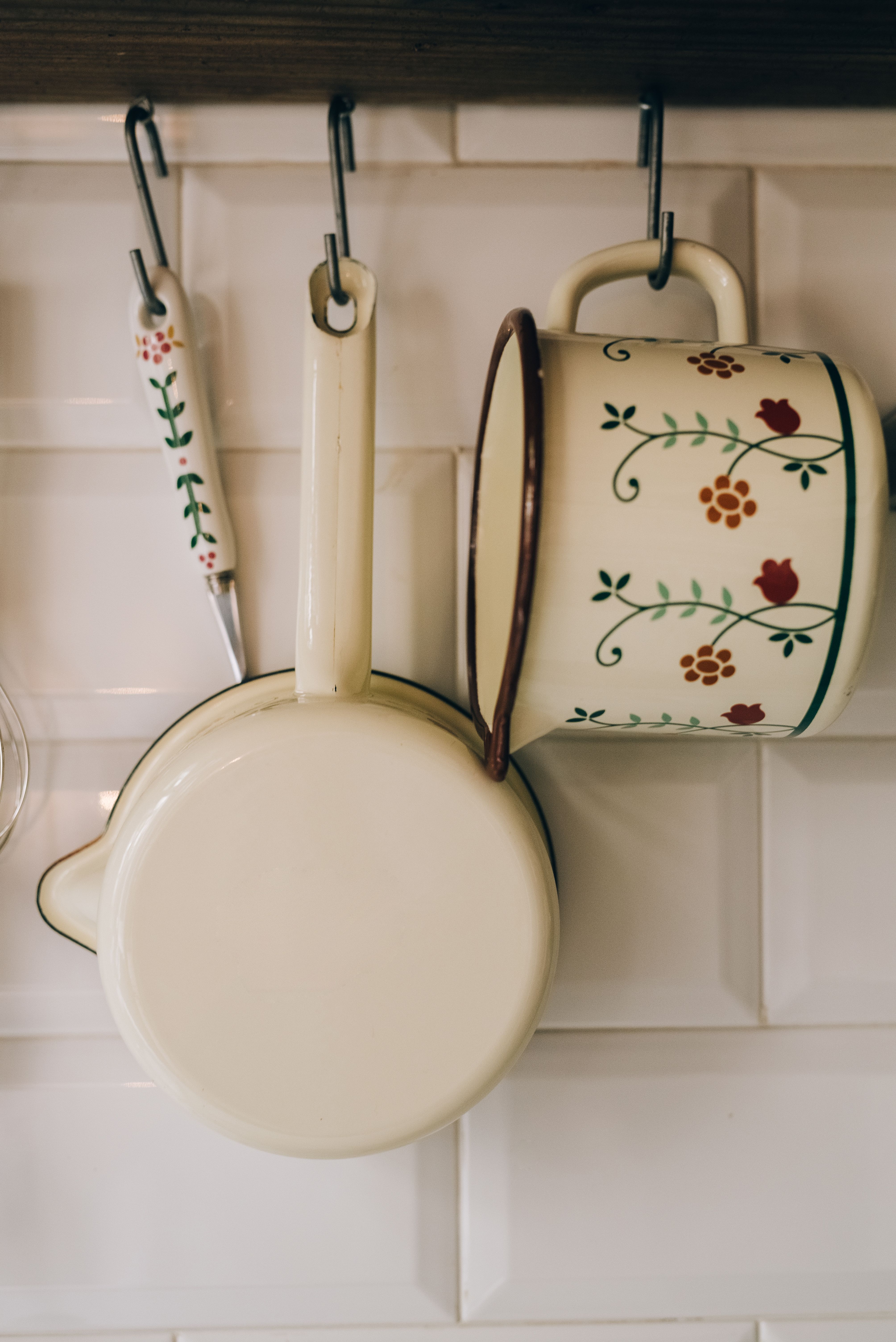 small brass wall hooks holding colorful ceramic coffee mugs under a shelf