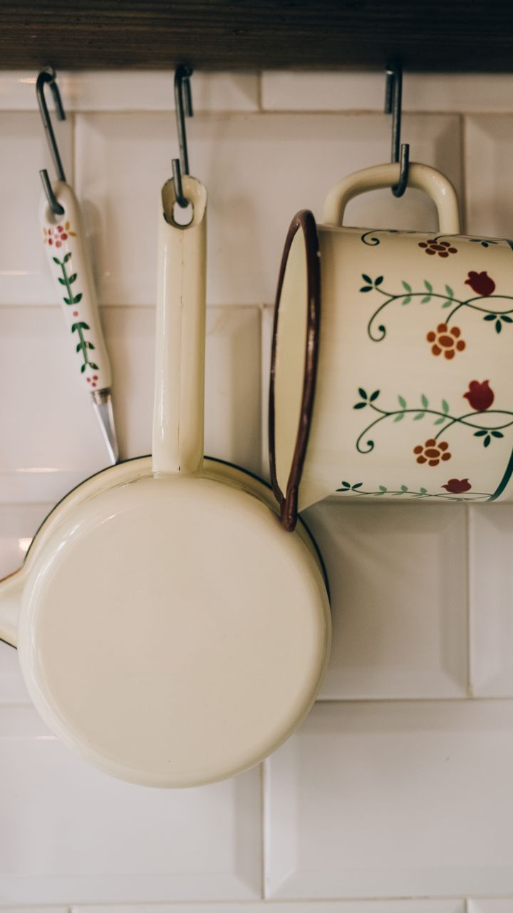 small brass wall hooks holding colorful ceramic coffee mugs under a shelf