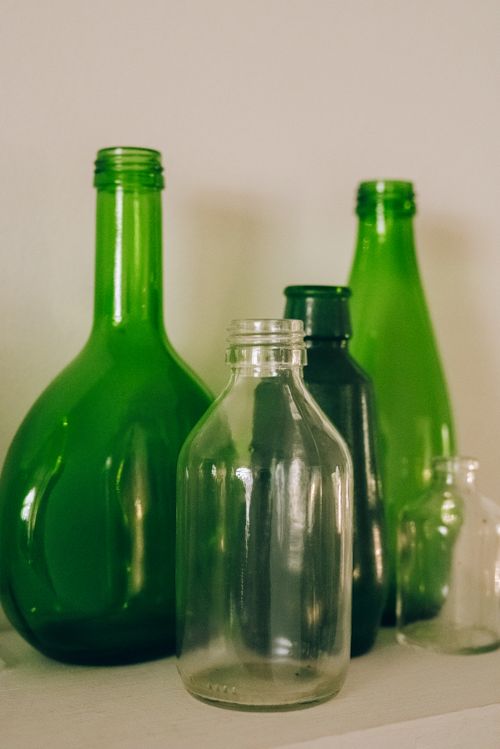 Free Collection of shiny green and transparent glass bottles on white table near wall Stock Photo