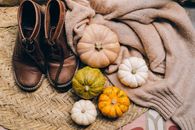Warm autumn composition with boots, pumpkins, and wool blanket on a woven mat.