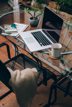 A cozy home office setup featuring a laptop, coffee mug, and decor on a glass table.