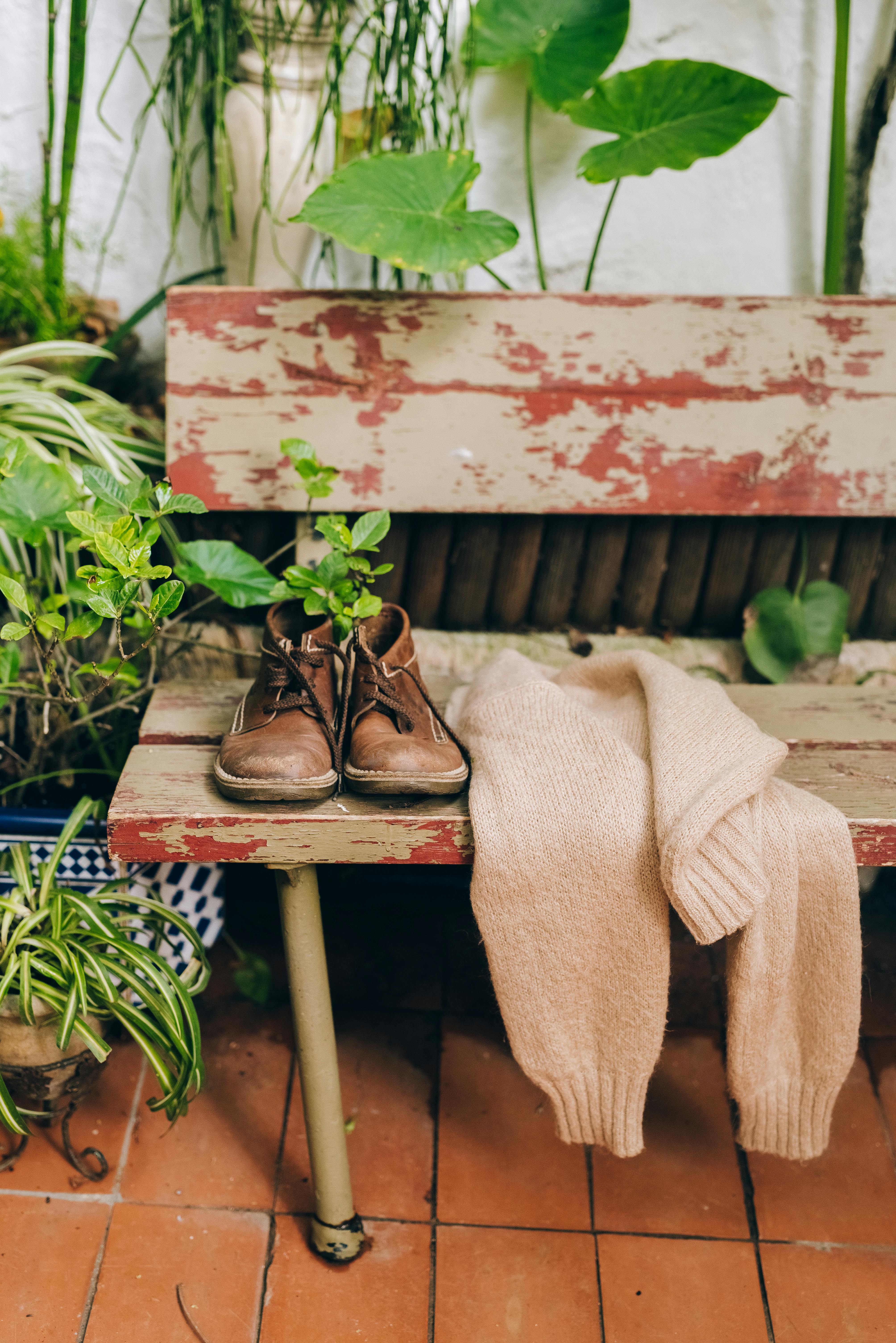 Rustic bench with brown shoes and sweater surrounded by lush plants