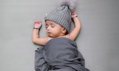 Free From above of adorable newborn child with closed eyes in bracelets napping on bed Stock Photo