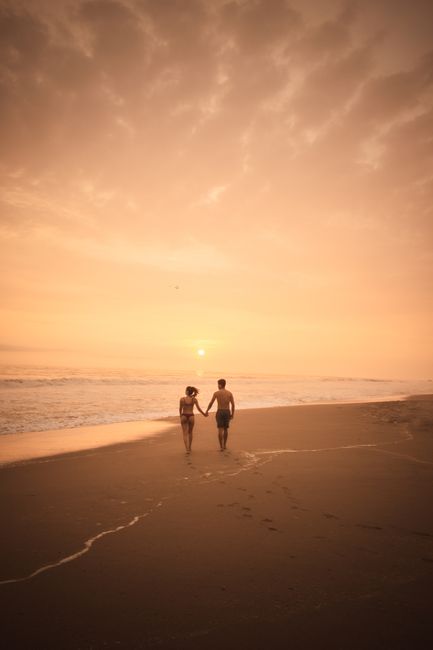 A couple holds hands as they walk along a Peruvian beach at sunset, creating a romantic ambiance.