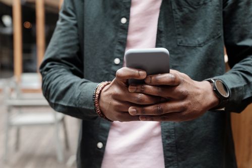 Free Close-up of person using smartphone indoors, showcasing casual fashion accessories. Stock Photo