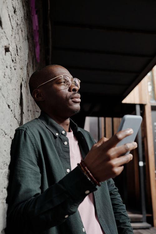 Free African American man with smartphone pondering against a concrete wall. Stock Photo