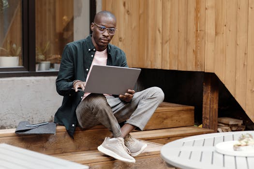 Young stylish man sitting outdoors, working on a laptop with a modern look.