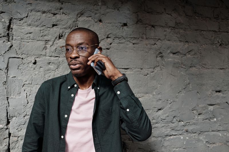 A Black man in glasses listens on a phone call.