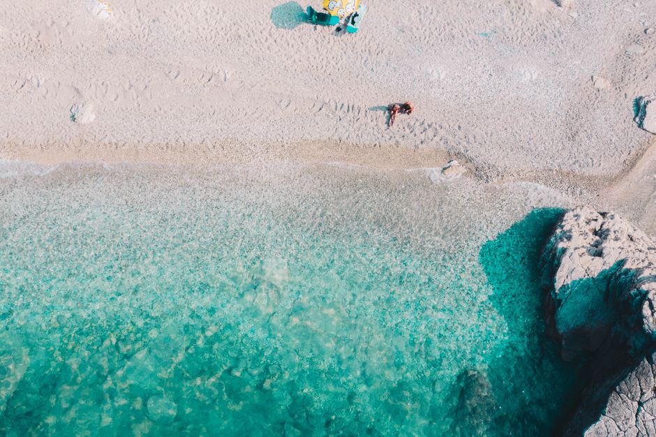 Breathtaking drone shot of a serene beach with turquoise waters and sunbathers enjoying the sun.