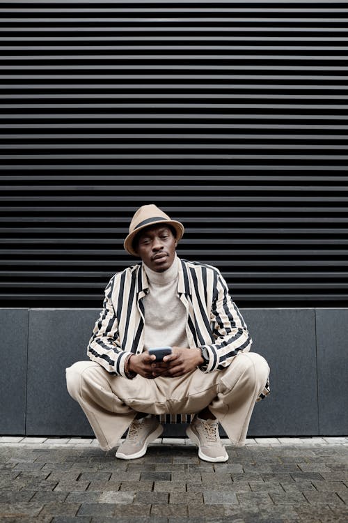 Man in Hat Squatting by Wall