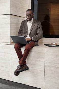 A stylish adult working on a laptop outside, showcasing modern fashion and professionalism.
