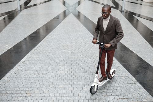 Free Stylish businessman riding an electric scooter on a modern paved outdoor area. Stock Photo