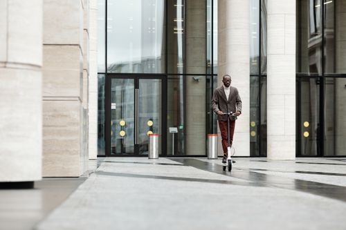 Free A stylish adult riding an electric scooter near office buildings in a city. Stock Photo