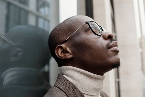 Free Stylish side profile of an African American man in a turtleneck and glasses, reflecting on a window. Stock Photo