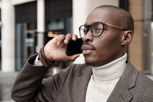 Free Man in Turtleneck Sweater Wearing Black Framed Eyeglasses Holding Black Smartphone Stock Photo
