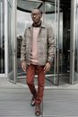 Man in Brown Leather Jacket and Red Pants Standing Beside Glass Door