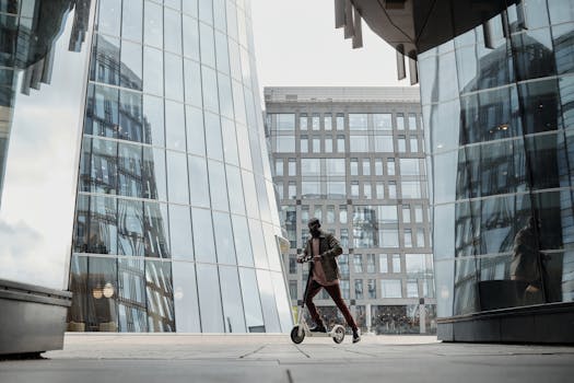 Person on scooter in modern cityscape with glass buildings reflecting urban lifestyle.