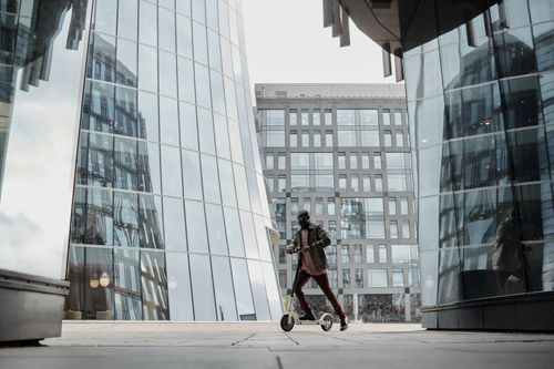 Free Person on scooter in modern cityscape with glass buildings reflecting urban lifestyle. Stock Photo