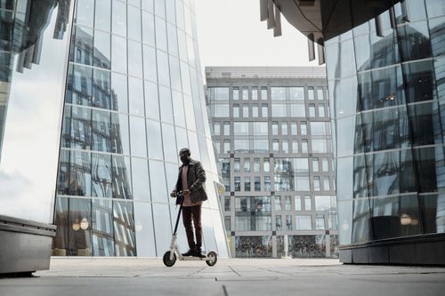 Free Man riding a scooter through an urban cityscape with reflective buildings highlighting modern commuting. Stock Photo