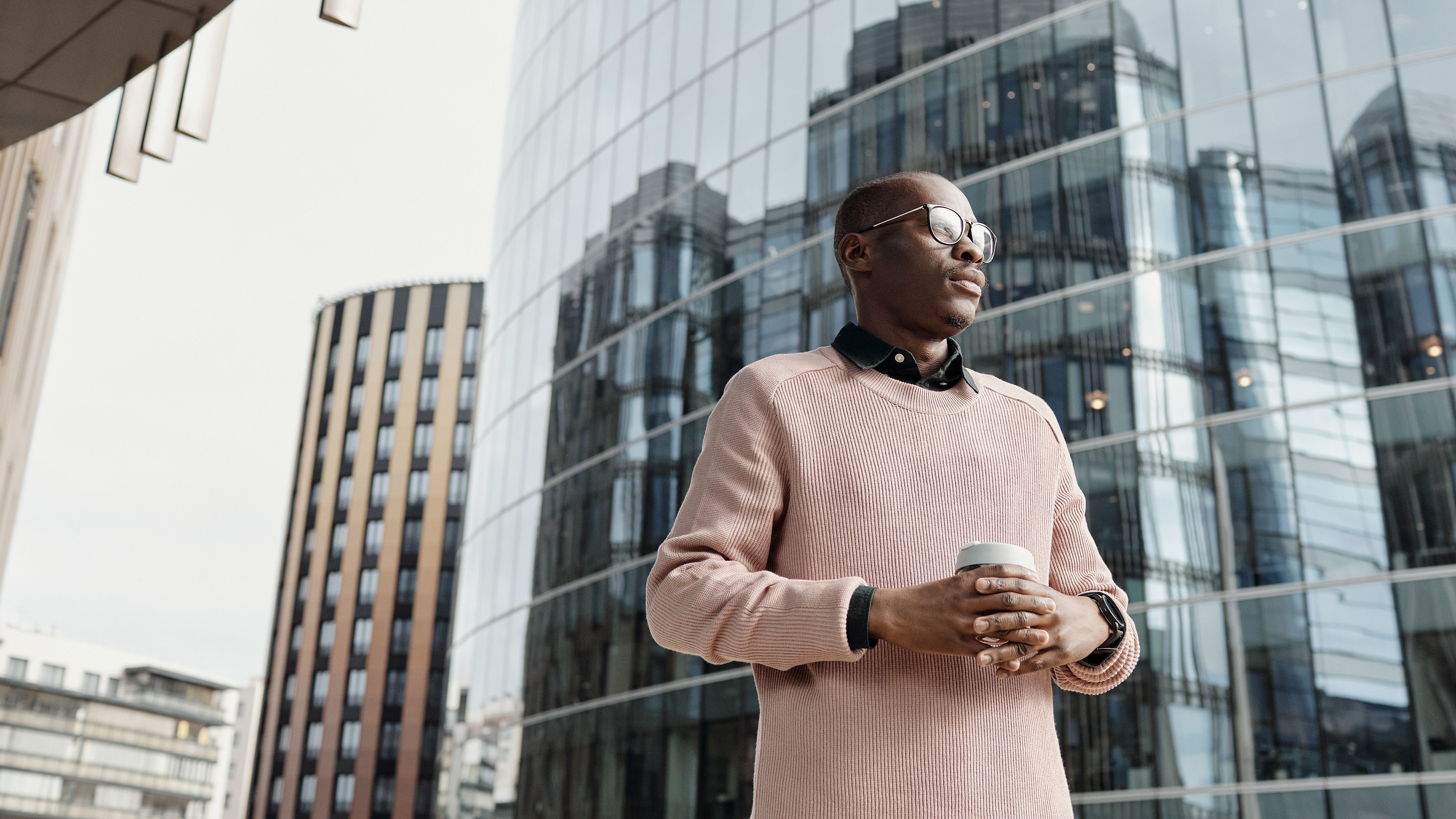 A man in a pink sweater standing at ease near modern glass buildings
