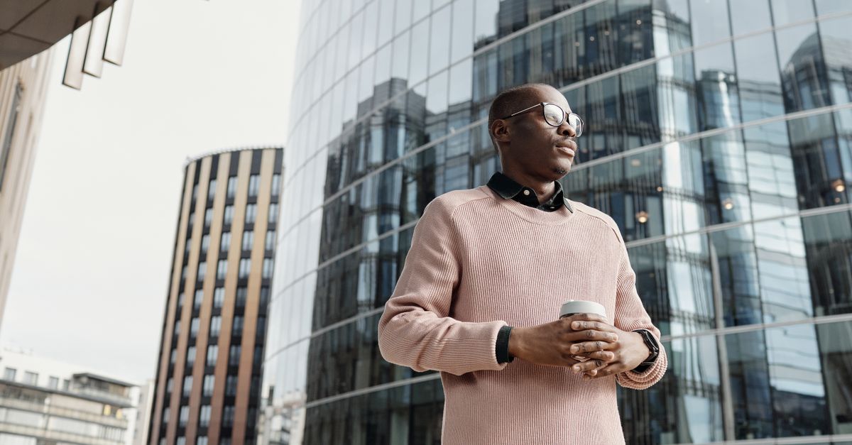 A man in a pink sweater standing at ease near modern glass buildings