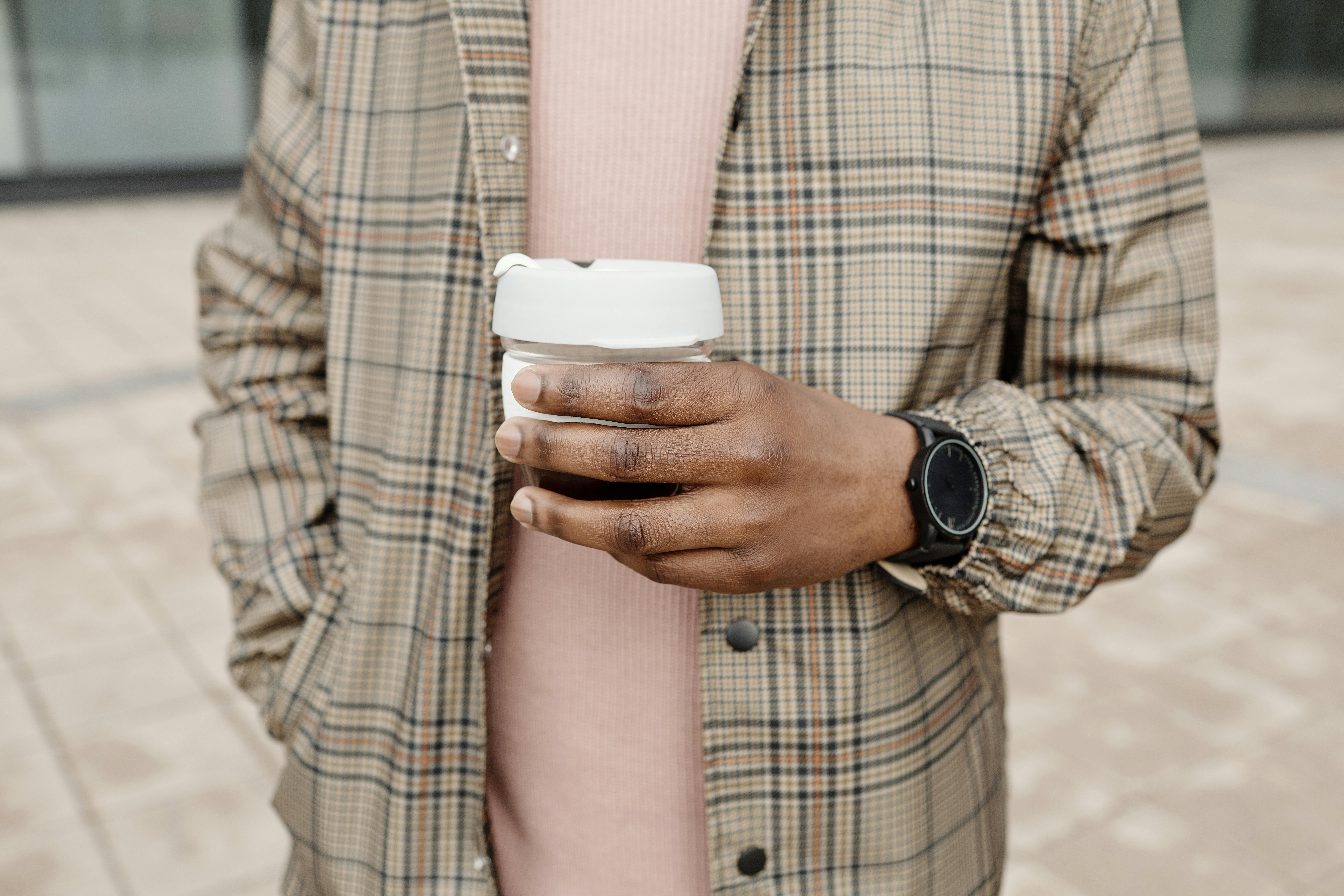 Close-up of a stylish individual in plaid holding a coffee cup and wearing a wristwatch.