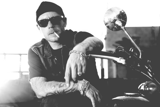 Black and white portrait of a man in sunglasses, smoking, sitting on a motorcycle.