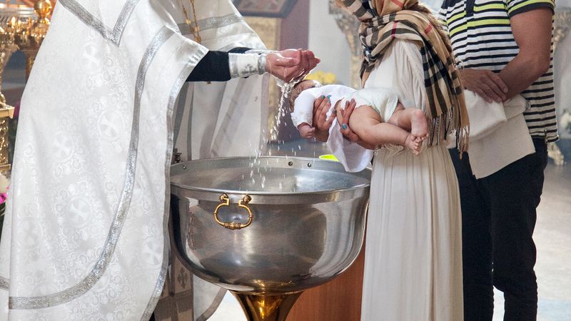 A priest performs a baptism ceremony on a baby in a church, witnessed by parents.