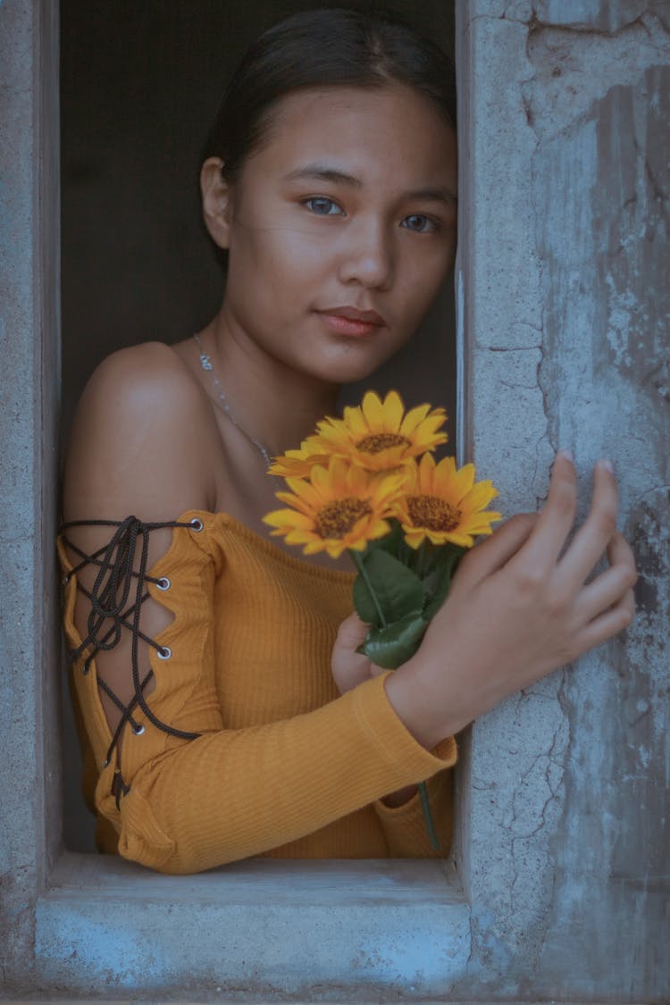 Teenage Girl With Bright Flowers Touching Concrete Wall