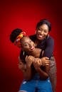 Happy African American women in casual clothes hugging and looking at camera against bright red background