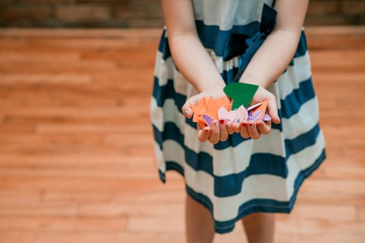 Child displaying colorful paper origami shapes in hands, indoors.