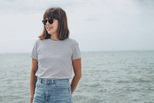 Free Woman Standing Near Sea While Wearing Black Frame Sunglasses Stock Photo