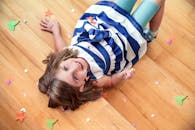 一个快乐的孩子躺在木地板上微笑，周围散落着五彩纸屑