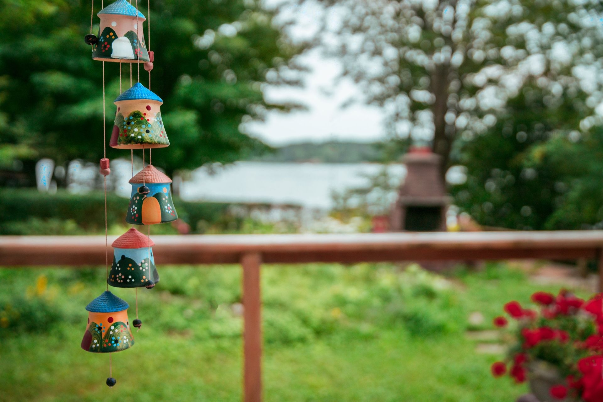Cute ceramic house ornaments hanging in a vibrant garden setting near water.