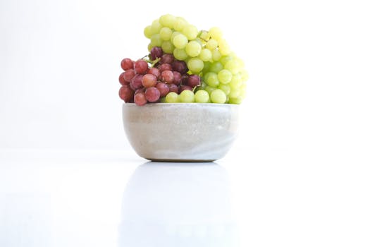 A minimalistic shot of fresh red and green grapes in a ceramic bowl on a white surface.