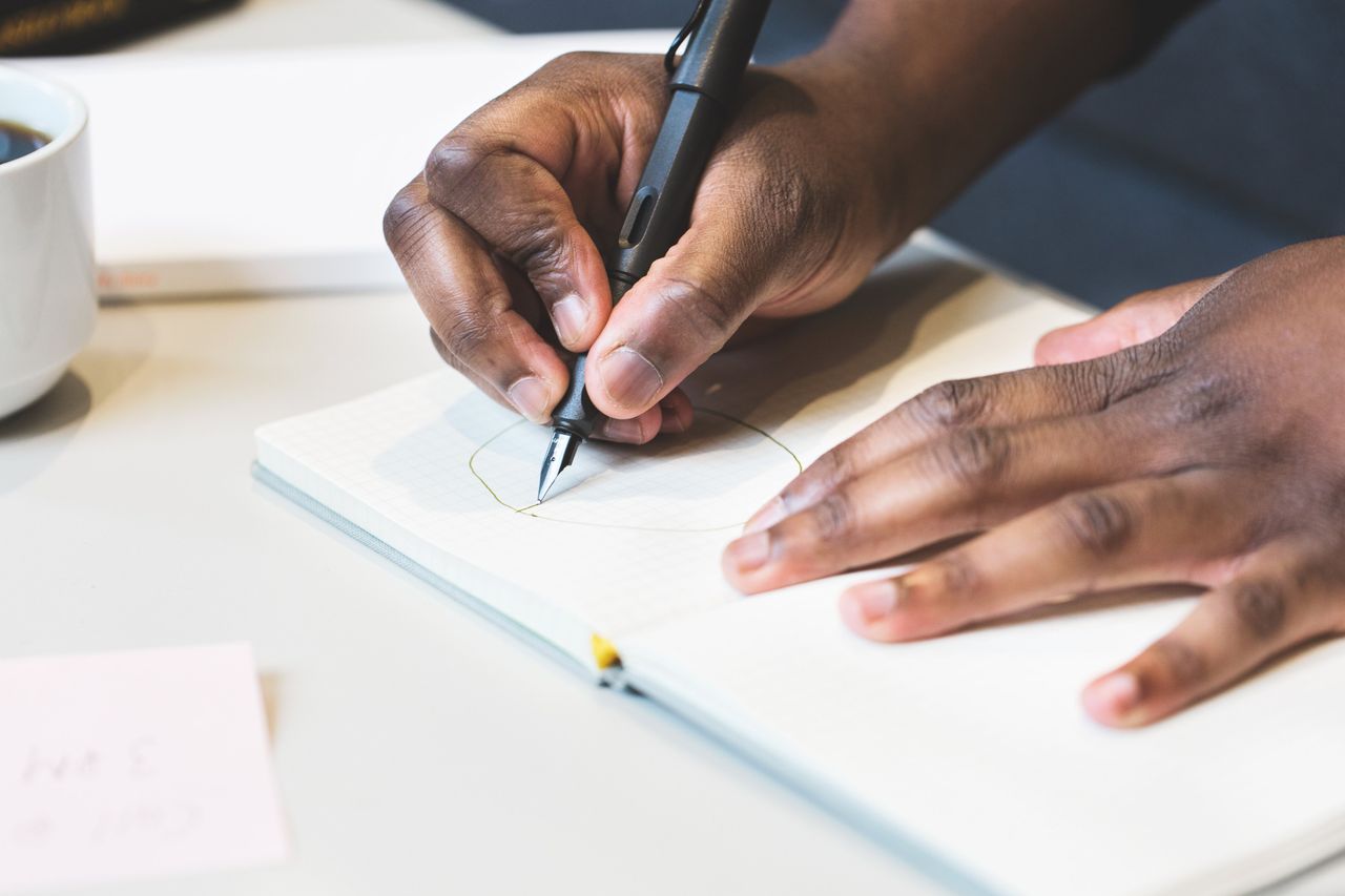 close up of a man writing with a fountain pen in a notebook indoors