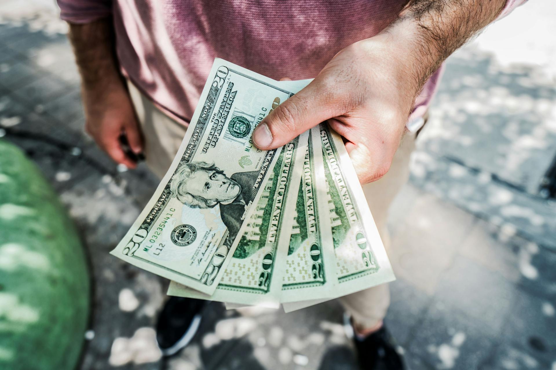 A person holding several twenty-dollar bills outdoors, depicting payment or financial transaction.