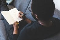 Man Sitting on Gray Couch Writing on White Book