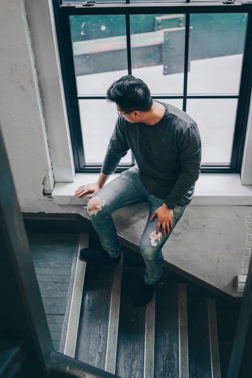 Man Sitting Beside Glass Window on Near Staircase