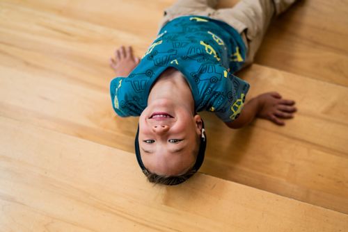 Free A cheerful child in a playful pose on a wooden floor, wearing a colorful shirt. Stock Photo