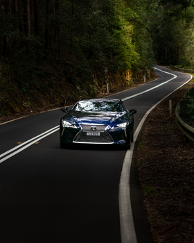 A luxury sports car drives through a winding forest road in Sydney, showcasing speed and elegance.