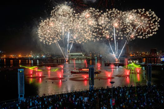 A vibrant fireworks display illuminates the city skyline and waterfront, captivating a large crowd.